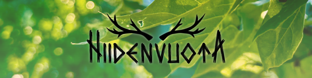 Hiidenvuota-logo mustalla tekstillä jonka päällä on sarvet, taustana on vihreä kuva lehdistä.